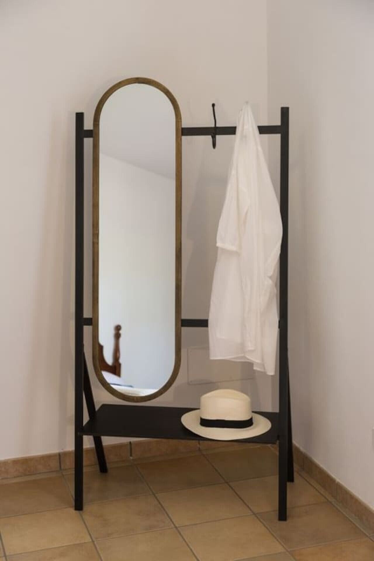 A mirror with a black frame and a white coat hanging on a black stand.