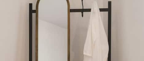A mirror with a black frame and a white coat hanging on a black stand.