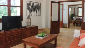A living room with a TV, wooden furniture, a plant on a table, and a dining area in the background. - Cottage `Es Pinaró` (Manacor)