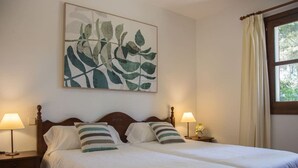 A double bed with white bedding and striped pillows, a wooden headboard, and a wall-mounted abstract painting. - Cottage `Es Pinaró` (Manacor)