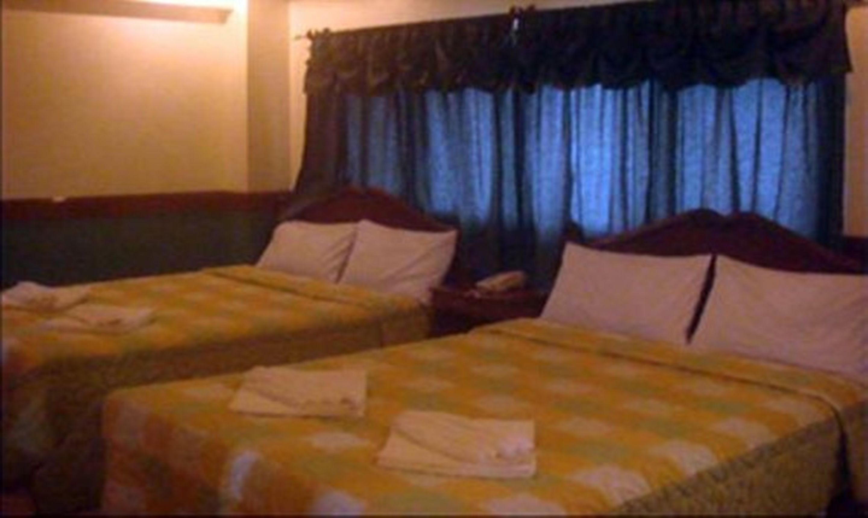Habitación de hotel con dos camas individuales, cada una con una almohada y una toalla doblada.