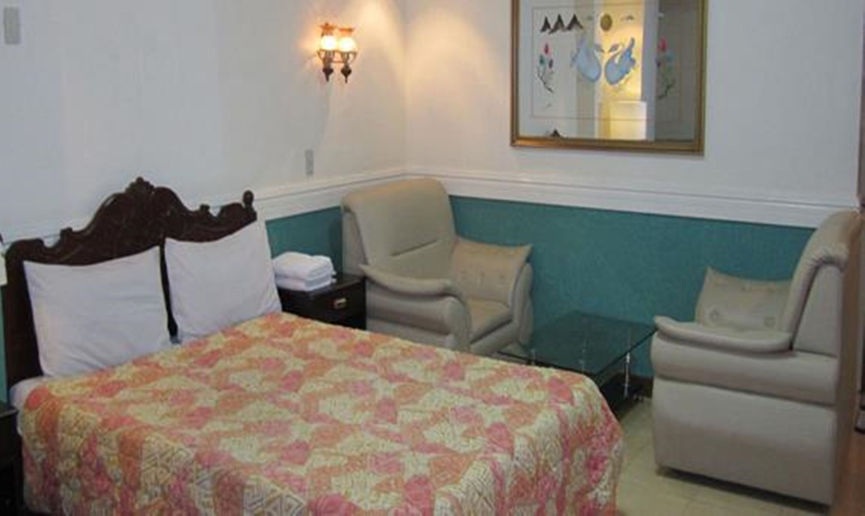 A hotel room with a bed, two armchairs, a small table, and a wall-mounted light fixture.