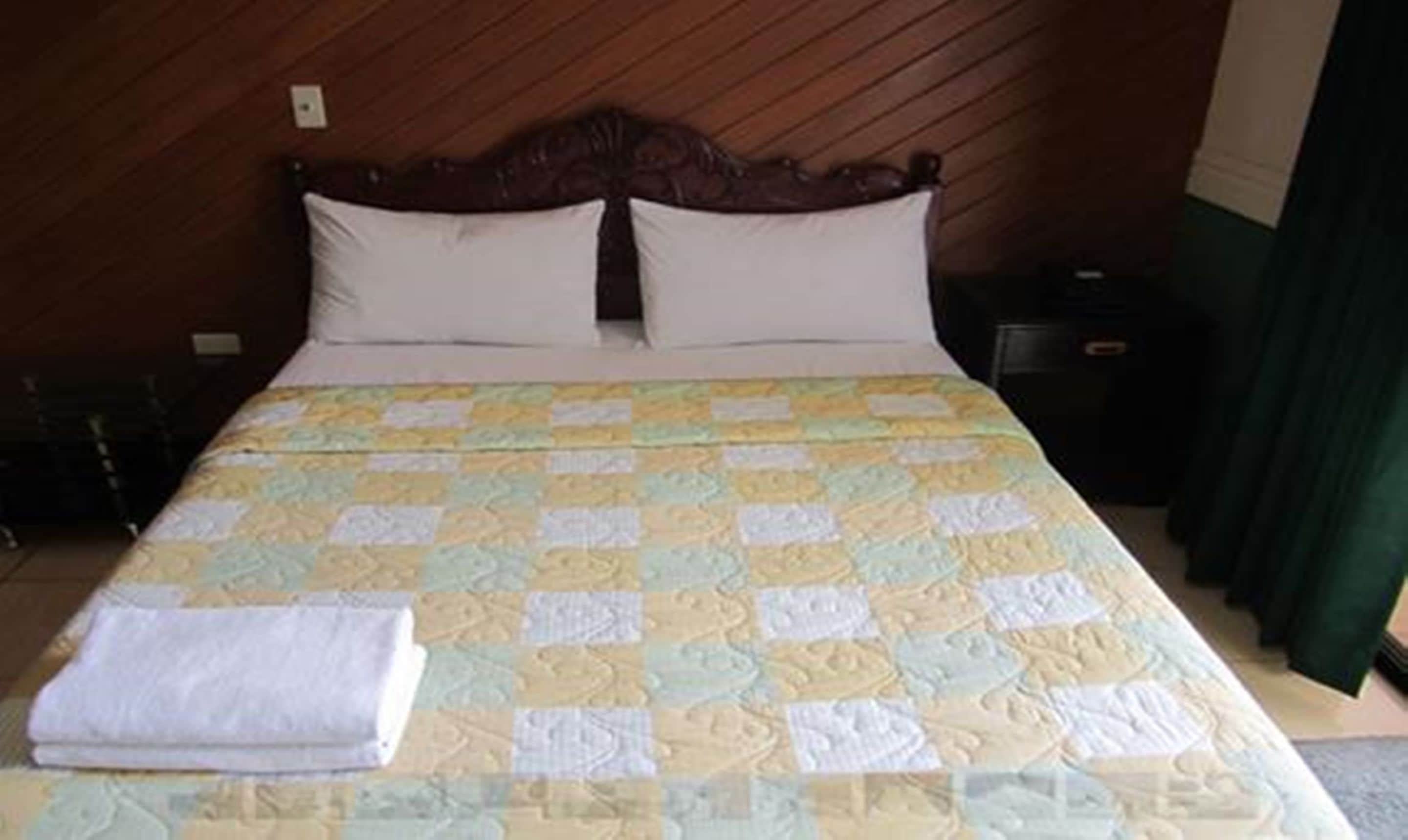 Una cama con una colcha acolchada, una almohada blanca y una toalla blanca doblada sobre la cama.