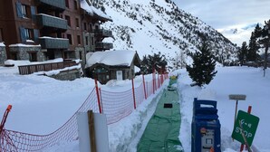 Un chemin enneigé, avec une bâche verte, une clôture rouge et une boîte de raccordement bleue.
