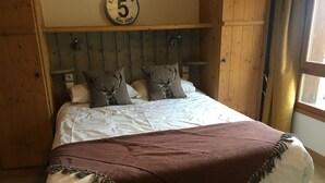 Un lit recouvert d’une couvre-lit blanche et marron, deux oreillers ornés de motifs de bois de cerf, et une tête de lit en bois avec une horloge.