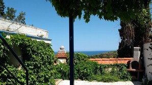 Un patio con dos sillas de plástico blanco, una mesa y vista al mar.