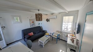 Un espacio habitable compacto con sofá, una mesita, una silla, televisión y ventana.