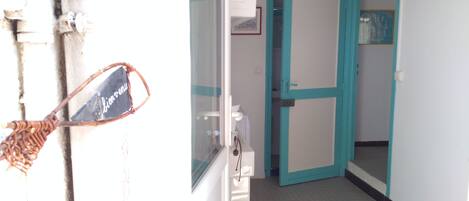 A hallway with a turquoise door, a white wall with a framed picture, and a door handle with a sign.