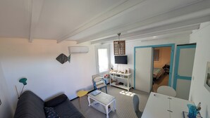 Una sala de estar con un sofá, una mesita, un televisor y una puerta que da a un dormitorio.