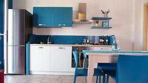 A modern kitchen with blue cabinets, a stainless steel refrigerator, and a dining area with blue chairs.