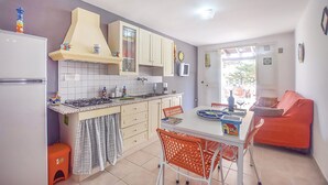 Cocina compacta con estufa a gas, armarios blancos y comedor con mesa y sillas.