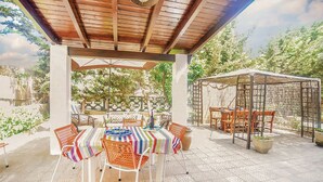 Un patio al aire libre con una pérgola de madera, un espacio de estar cubierto y una mesa con sillas.