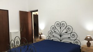Un dormitorio con cama, mesita de noche, lámpara y puerta.