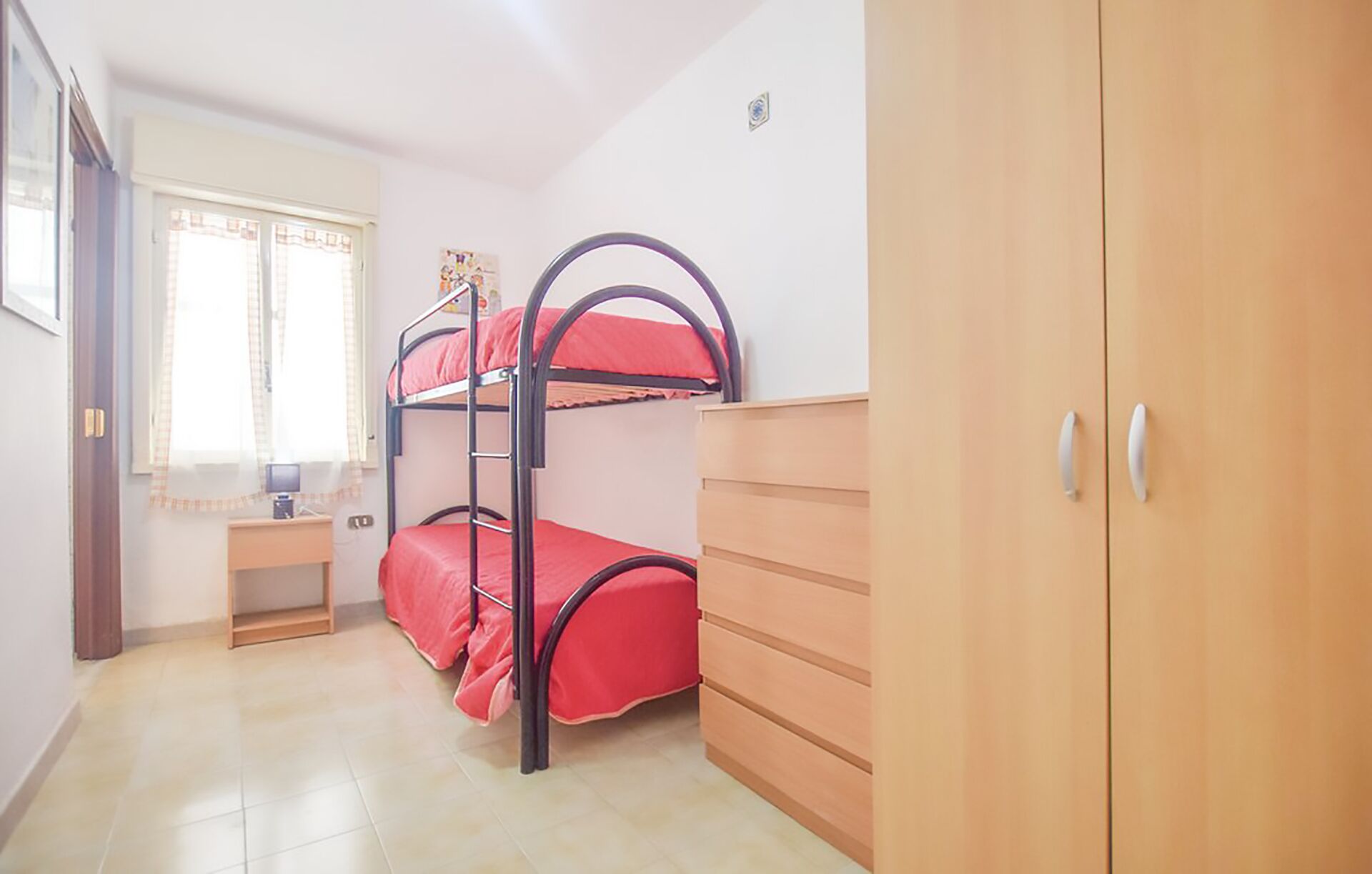 Een slaapkamer met een stapelbed, bureau, garderobe en raam met gordijnen.