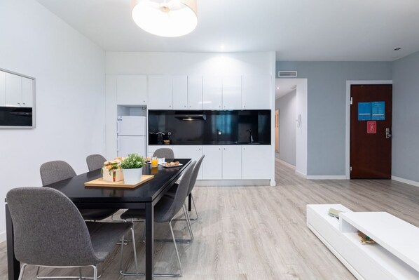 A modern kitchen with white cabinets, a black countertop, and a dining area with a black table and grey chairs. - A (VA012.2) TH Ayuntamiento 1B (Valencia / València)