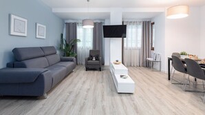 A modern living room with a grey sofa, a white coffee table, and a dining area with a table and chairs.