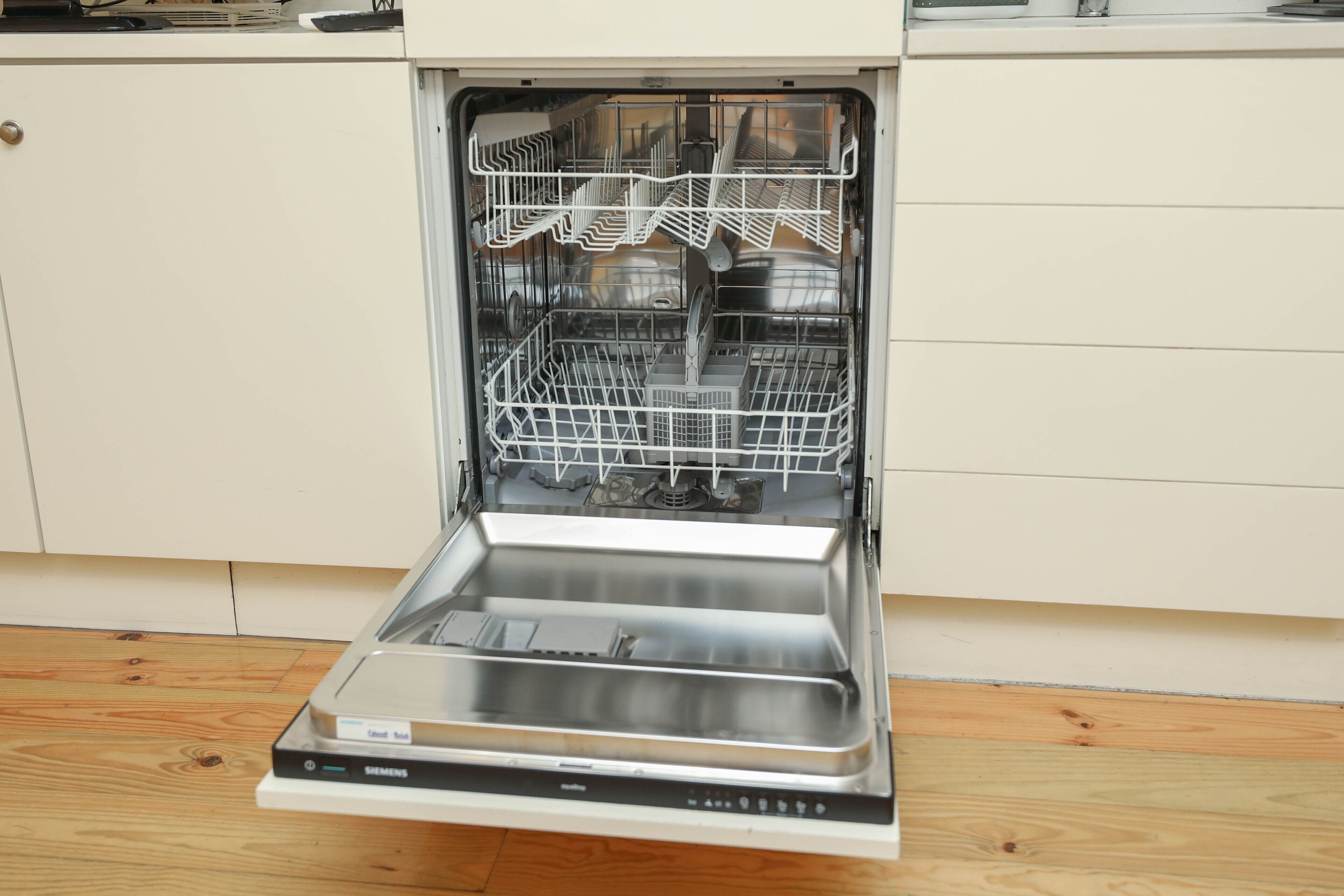 An open dishwasher with a stainless steel interior and a control panel.