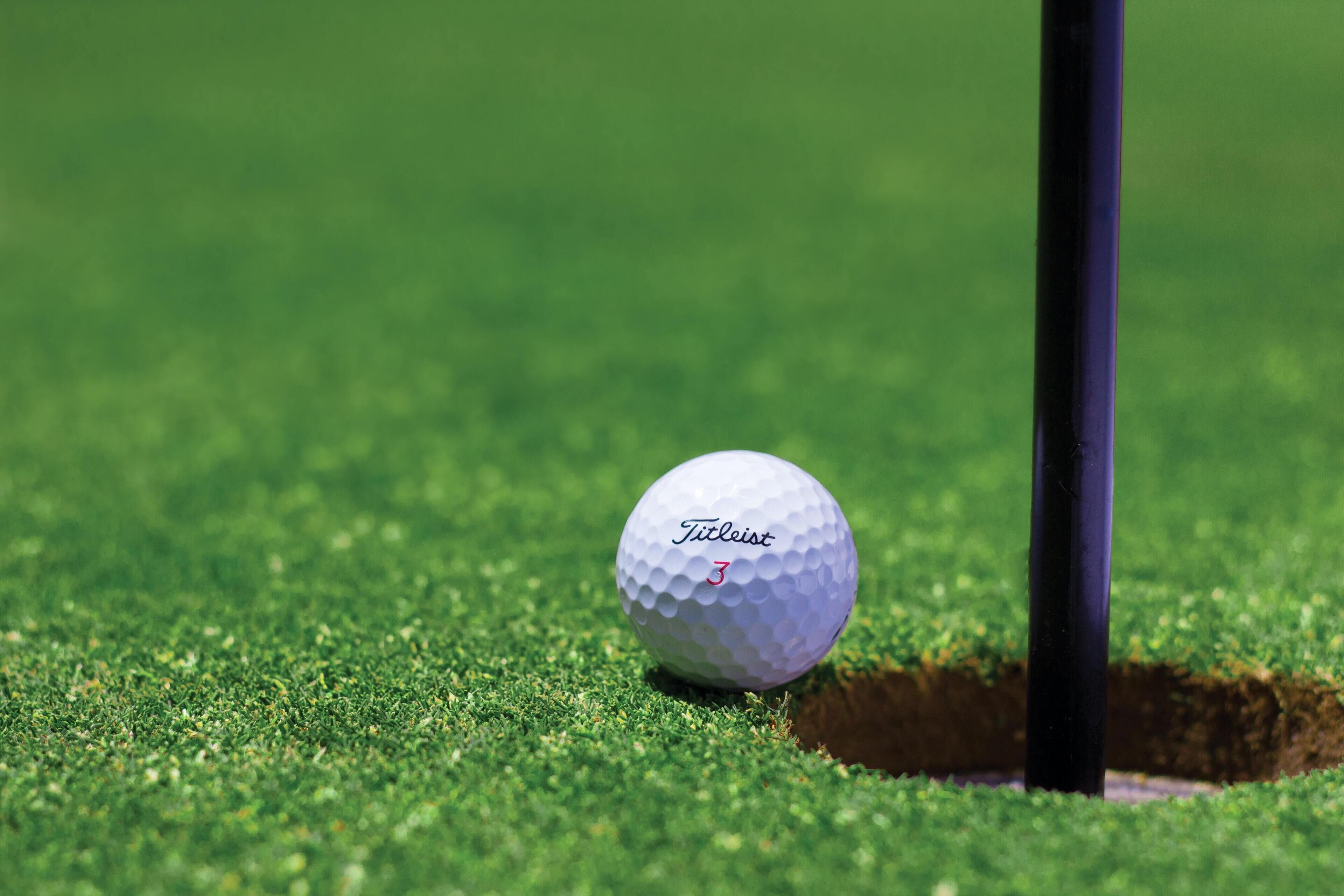 Una pelota de golf cerca de un hoyo en un campo verde.