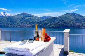 A poolside area with a view of mountains, a bottle of champagne, glasses, a bouquet of red roses, and a stack of towels. - Casa Laura Apt. 6, Plesio, Italy (Plesio)