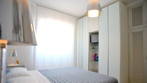 Ein Schlafzimmer mit einem Bett, einem Nachttisch, einer Lampe, einem Kleiderschrank und einem Fernseher auf einem Regal.