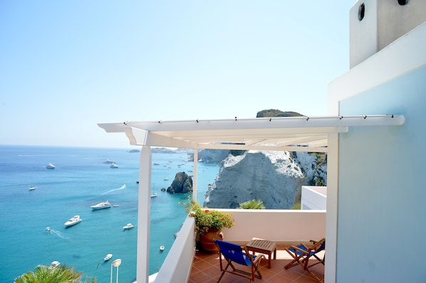 A balcony with a view of the sea, a white pergola, a potted plant, and a table with chairs.