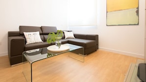 Ein modernes Wohnzimmer mit einem braunen Ledersofa, einem Glastisch und einem minimalistischen abstrakten Gemälde an der Wand.
