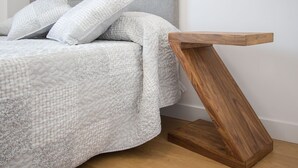 Ein Bett mit grauem Kopfteil und weißer Bettwäsche, ein Holznachttisch und Holzboden.