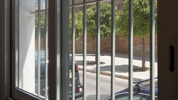 Ein Fenster mit vertikalen Gitterstäben, Blick auf eine Straße mit parkenden Autos und ein entferntes Gebäude mit einem Turm.
