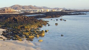 A beach with clear water, rocky shoreline, and footprints in the sand. - VILLA MONTAÑA COLORADA (Lajares)