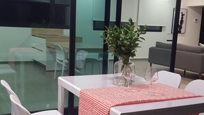 A dining area with a table set for two, white chairs, a glass partition, and a view into a kitchen area. - VILLA MONTAÑA COLORADA (Lajares)
