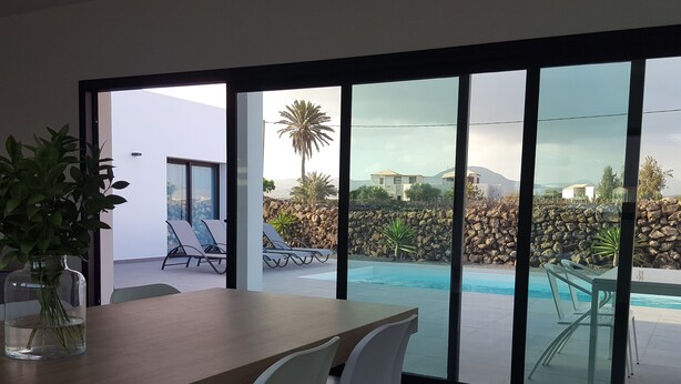 A modern dining area with a view of a swimming pool and a stone wall. - VILLA MONTAÑA COLORADA (Lajares)