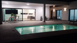 A modern indoor pool area with a glass-enclosed dining area, a sofa, and a seating area with chairs. - VILLA MONTAÑA COLORADA (Lajares)