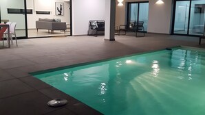 An indoor swimming pool with a clear view of the adjacent living area, including a sofa and chairs. - VILLA MONTAÑA COLORADA (Lajares)