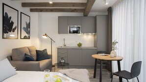 Une chambre d’hôtel moderne comprenant un lit, un canapé, une table à manger avec des chaises, un coin cuisine avec un four à micro-ondes et une grande fenêtre avec des rideaux.