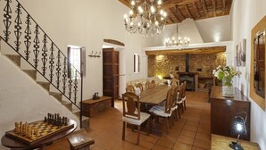 Un comedor espacioso con una gran mesa de madera y sillas, una araña y una escalera con barandillas decorativas.