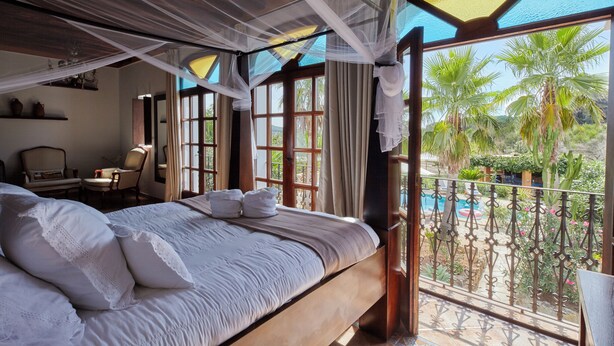 Un dormitorio con una cama grande, un balcón con piscina y vistas a palmeras.