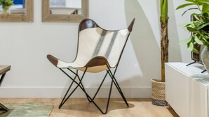 Une pièce avec un plancher en bois, une chaise dotée d’un coussin à rayures et une grande plante.
