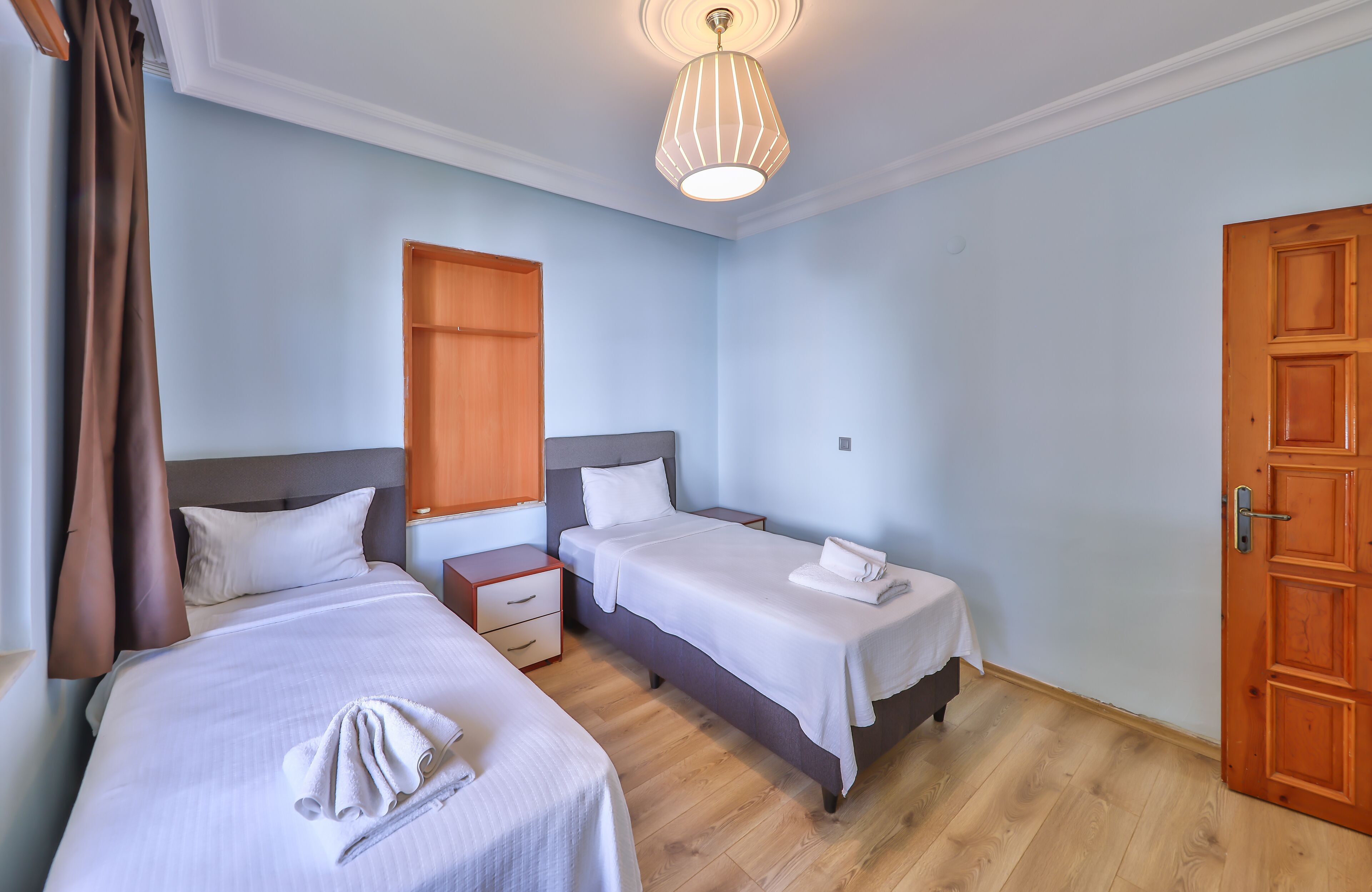Une chambre d’hôtel avec deux lits, un plancher en bois, un luminaire au plafond et une porte en bois.