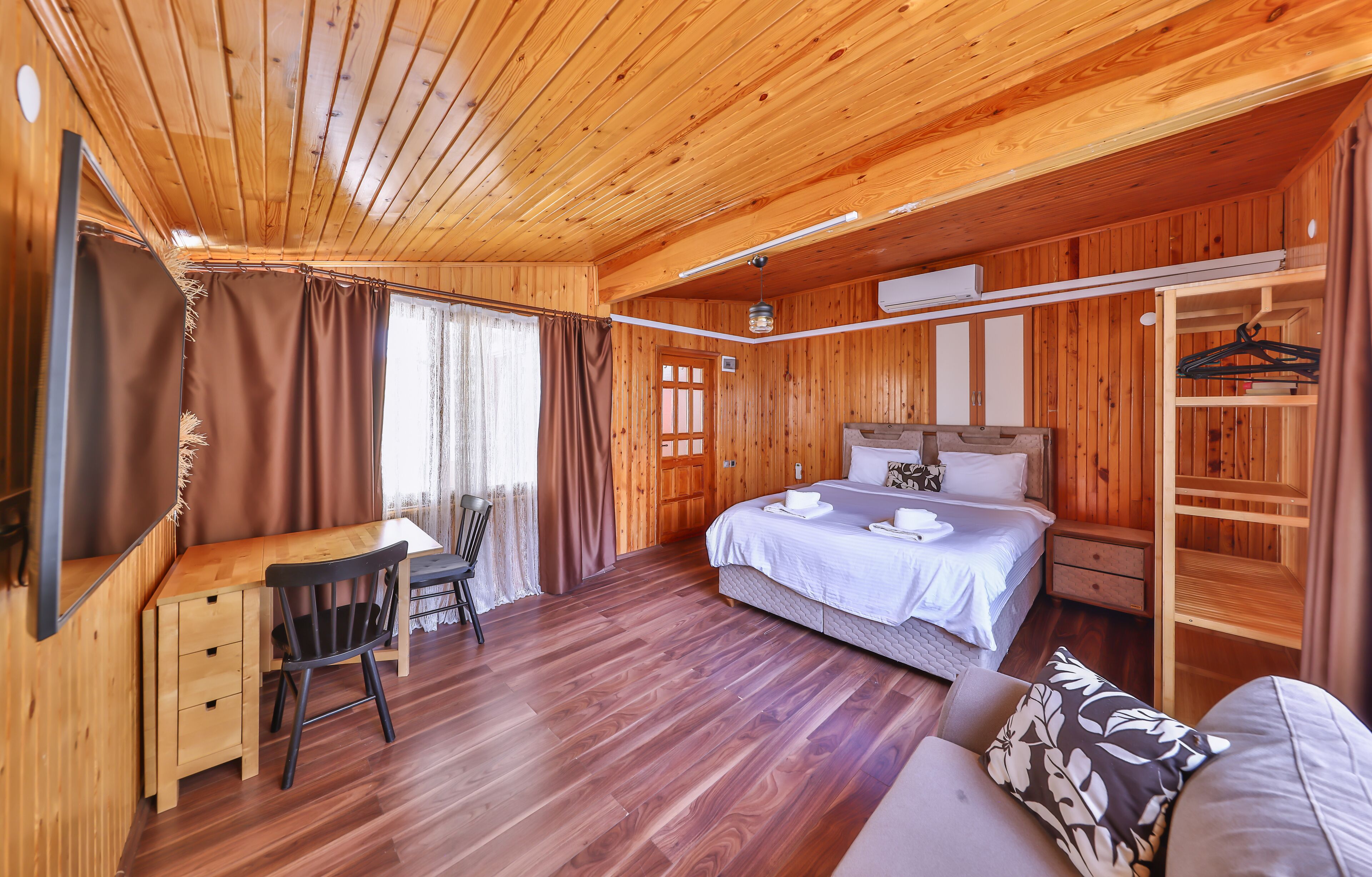 Ein Zimmer in einer Holzhütte mit Bett, Schreibtisch, Stuhl und einer Garderobe.