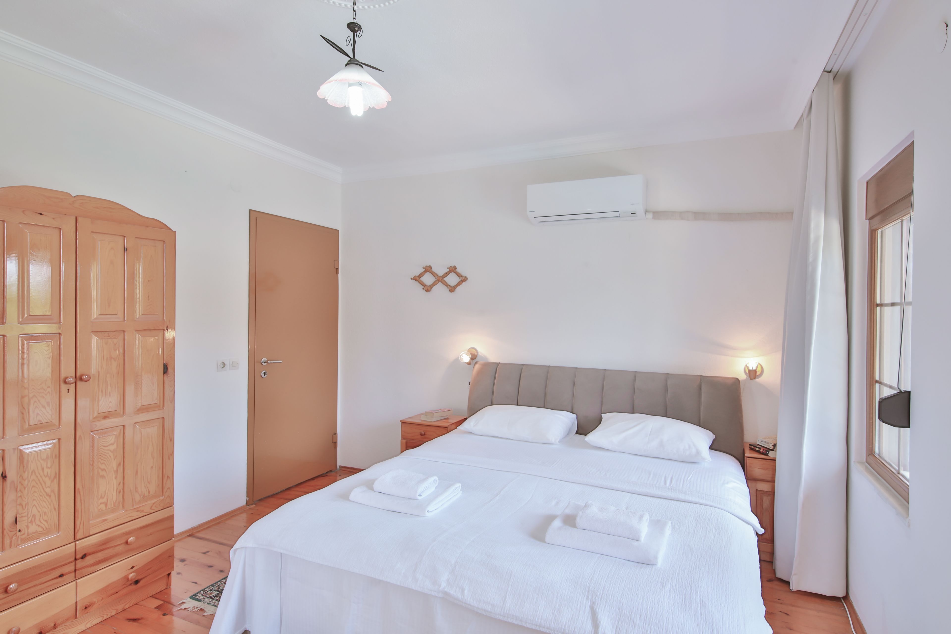 Une chambre avec un grand lit, une armoire en bois et un appareil de climatisation.