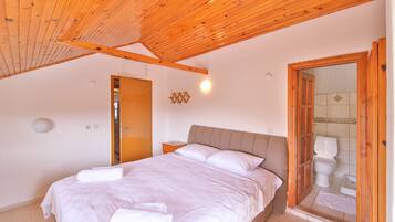 A bedroom with a wooden ceiling, a bed with white linens, a nightstand, and a bathroom with a toilet and shower.