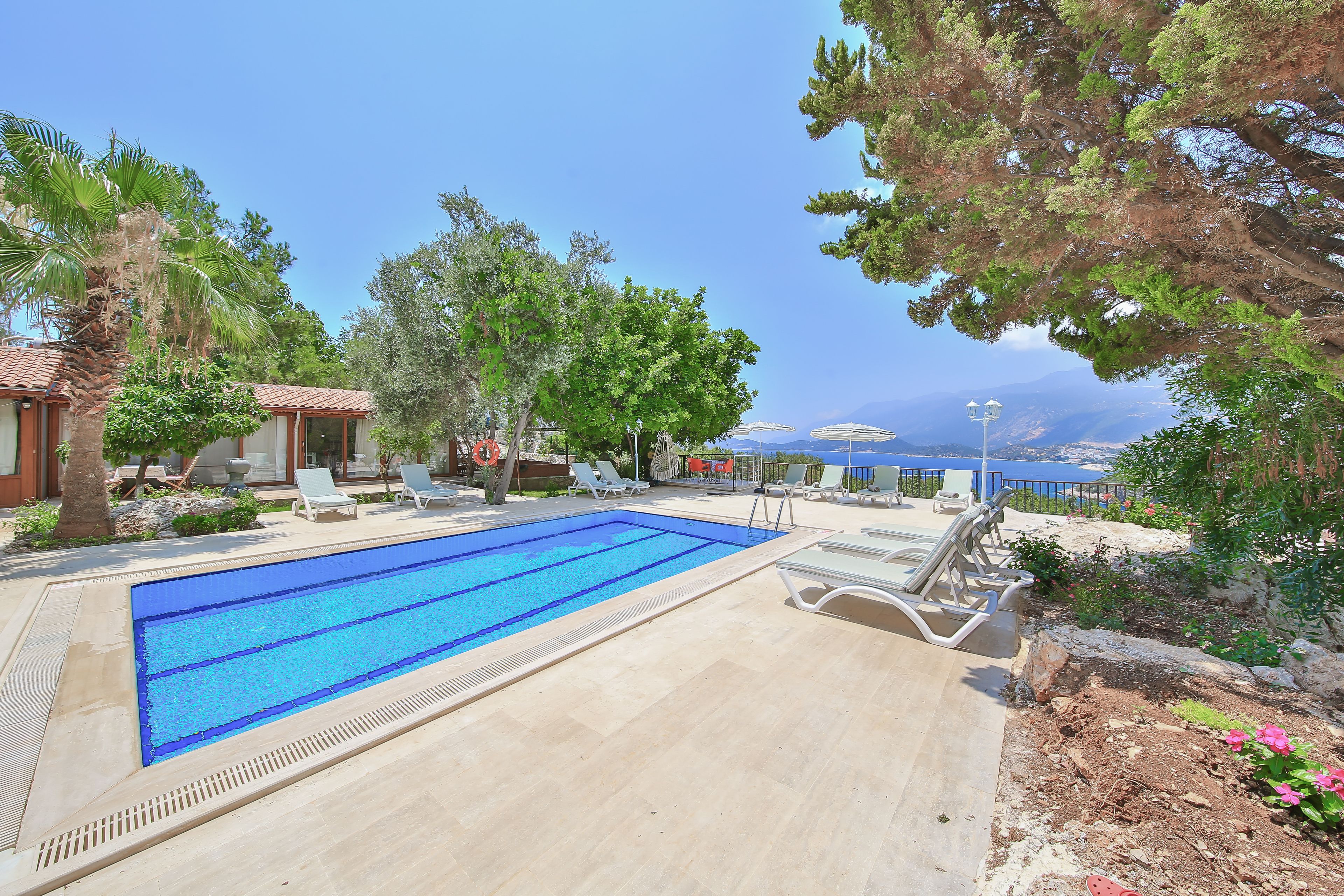 A swimming pool with lounge chairs, surrounded by trees and a view of the sea.