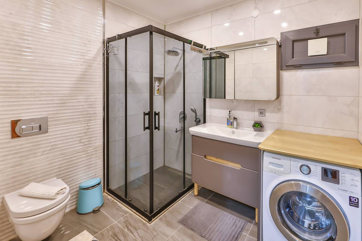 Un baño moderno con ducha de vidrio, inodoro, lavadora y lavabo con espejo superior.