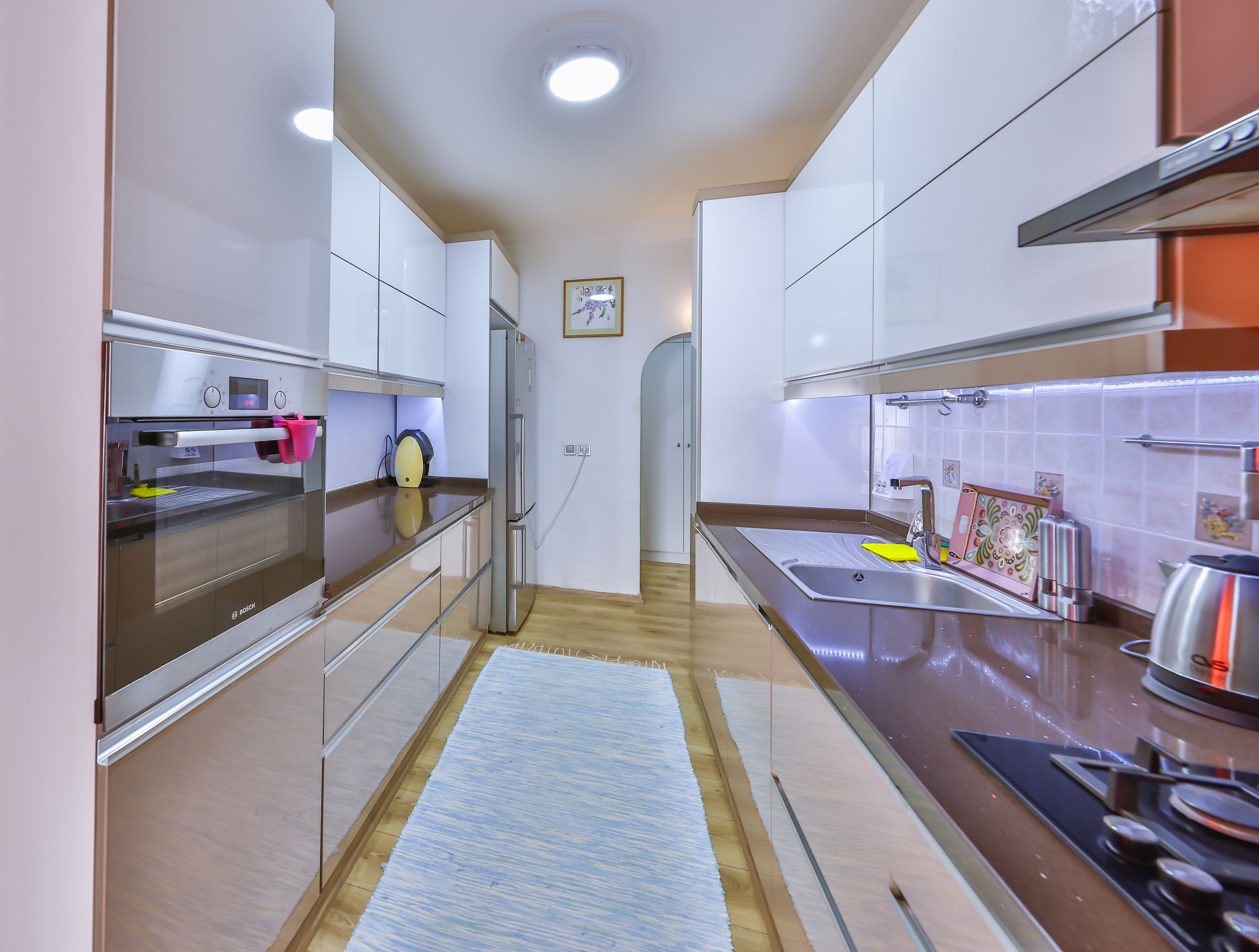 A modern kitchen with stainless steel appliances, a wooden floor, and a blue rug.