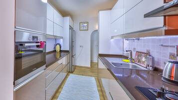 A modern kitchen with stainless steel appliances, a wooden floor, and a blue rug.