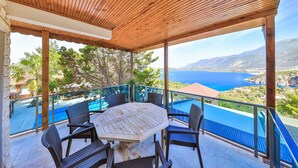 A covered outdoor seating area with a wooden ceiling, overlooking a scenic view of the sea and mountains. - Villa Dundar Kas Apartments (Kas)
