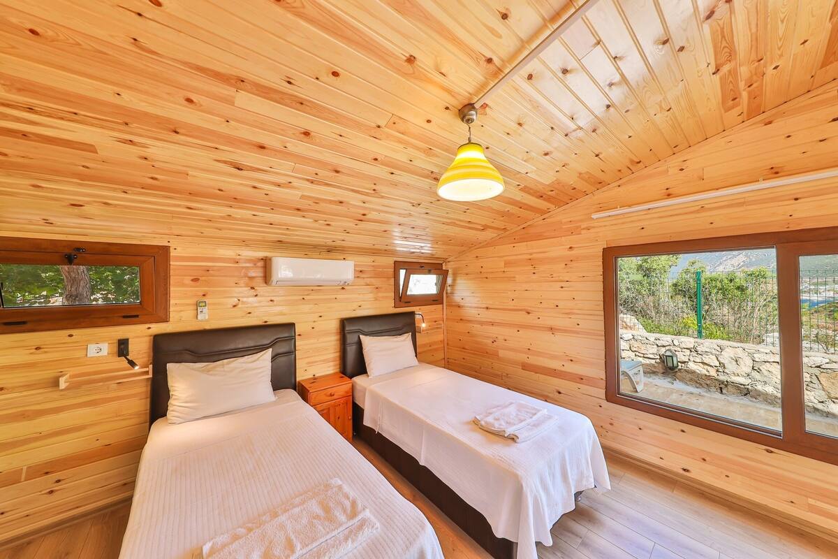 Habitación de cabaña de madera con dos camas, una lámpara en el techo y un gran ventanal con vistas al exterior.