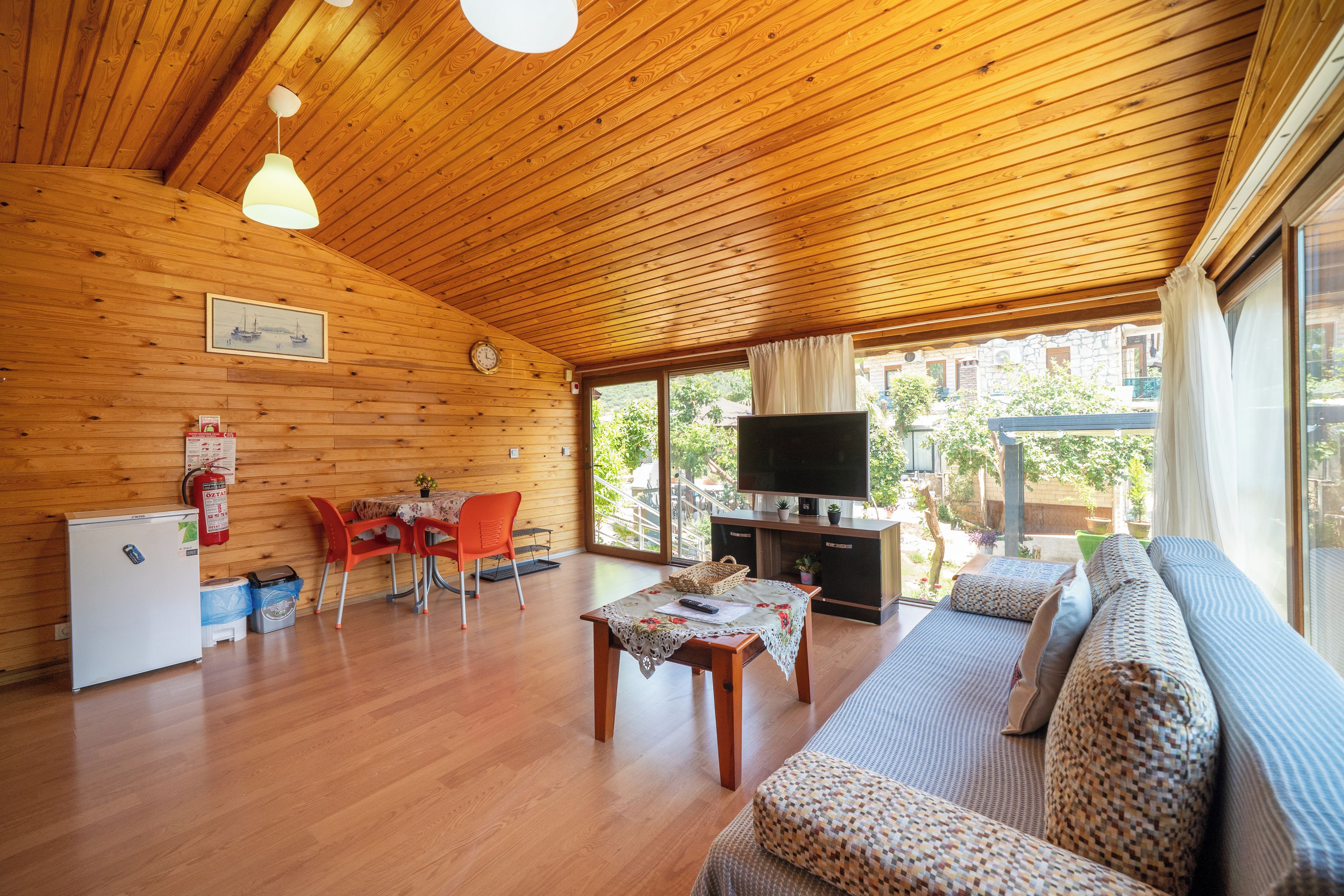 A wooden interior with a dining area, sofa, TV, and a view of the outdoors.