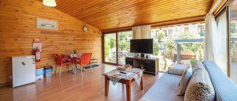 A wooden interior with a dining area, sofa, TV, and a view of the outdoors.