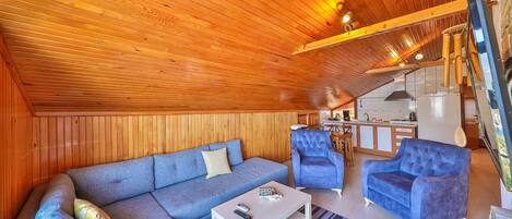 Una sala acogedora con techo de madera, un sofá, una mesa de centro y dos sillones.